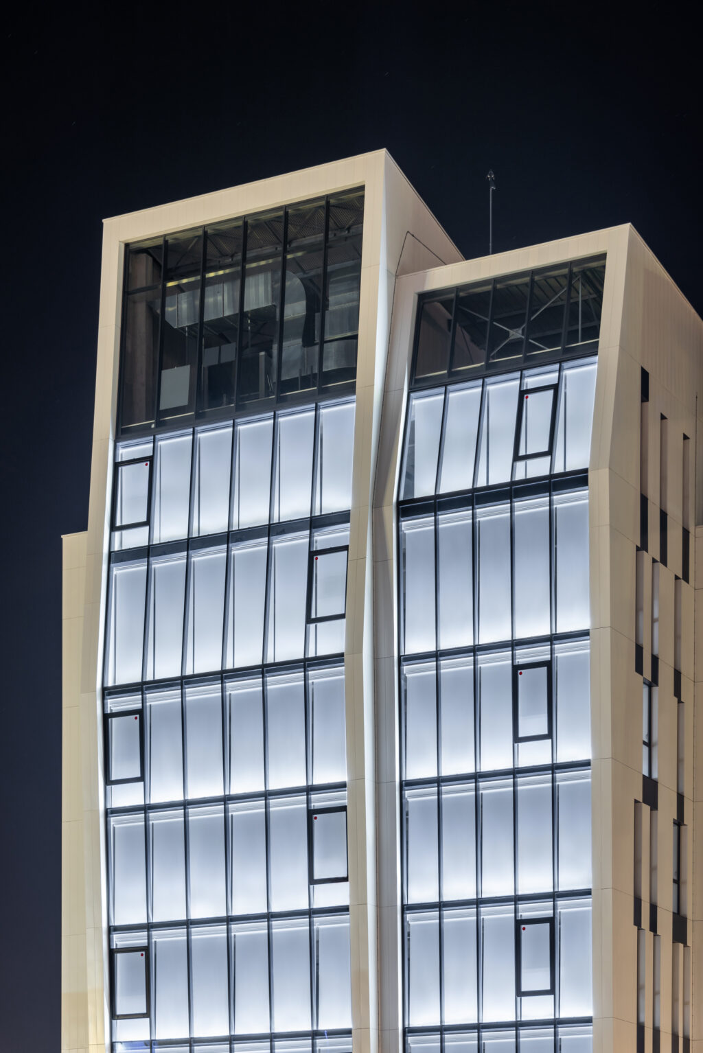 Façade vitrée du projet Initial Grand Parilly éclairée de nuit, équipée d’une solution textile Soltis Touch pour le confort visuel.