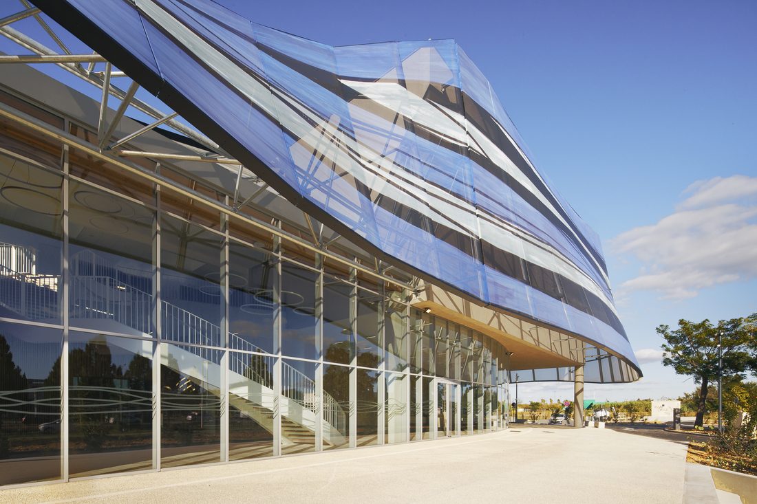 Wide view of Sport Hall Nîmes with full printed mesh façade in blue and white tones.