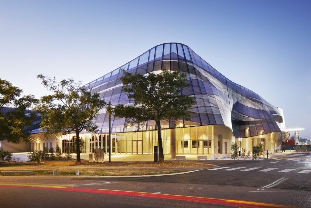 Curved exterior view of Sport Hall Nîmes with printed mesh façade at twilight.