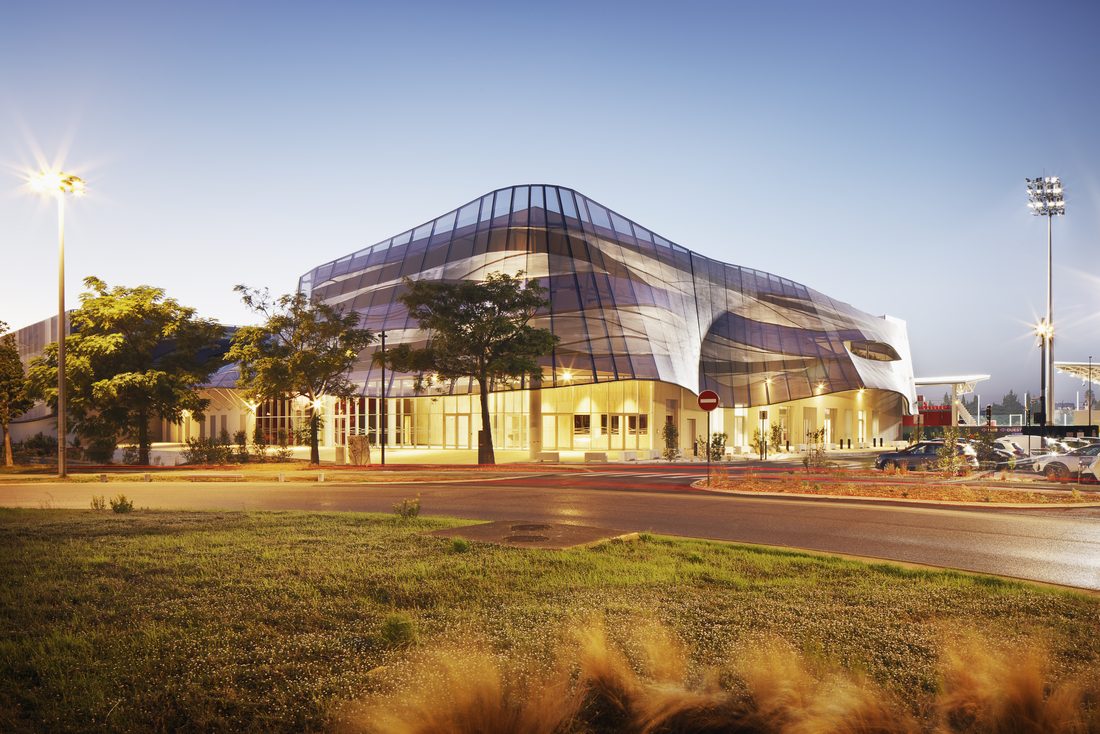 Street view of Sport Hall Nîmes featuring its flowing blue and white mesh façade.