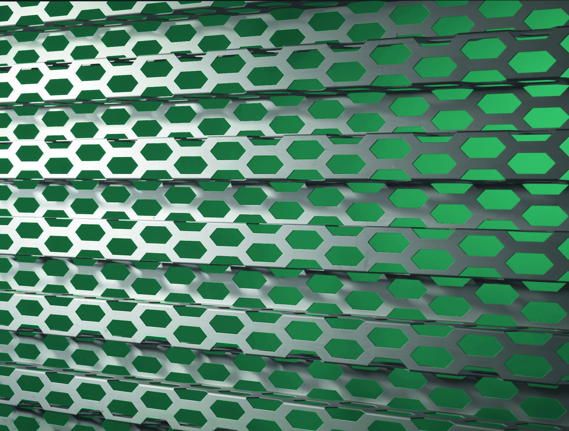 Gros plan d’une façade métallique perforée avec motifs hexagonaux, laissant apparaître un fond vert en arrière-plan.