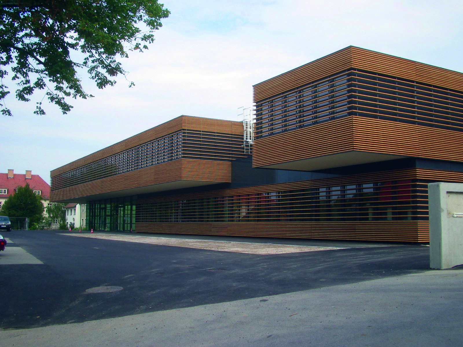 Bâtiment contemporain à volumes rectangulaires, habillé de lames horizontales brun-cuivré, avec de larges vitrages en façade.