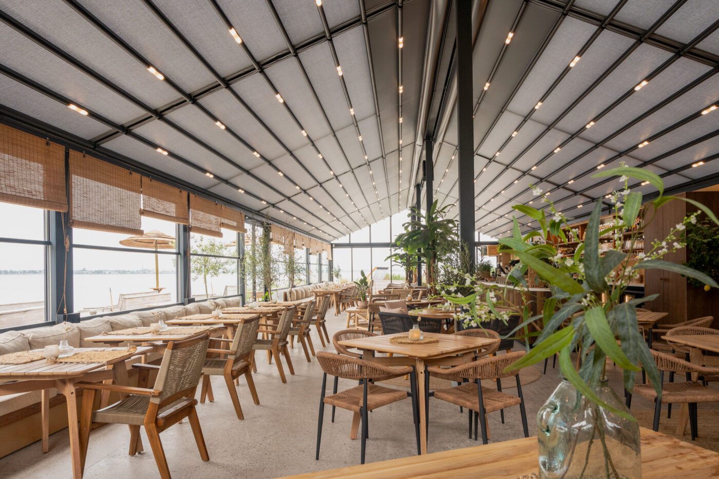 Intérieur lumineux d’un restaurant de plage avec toiture textile et mobilier bois face à la mer.