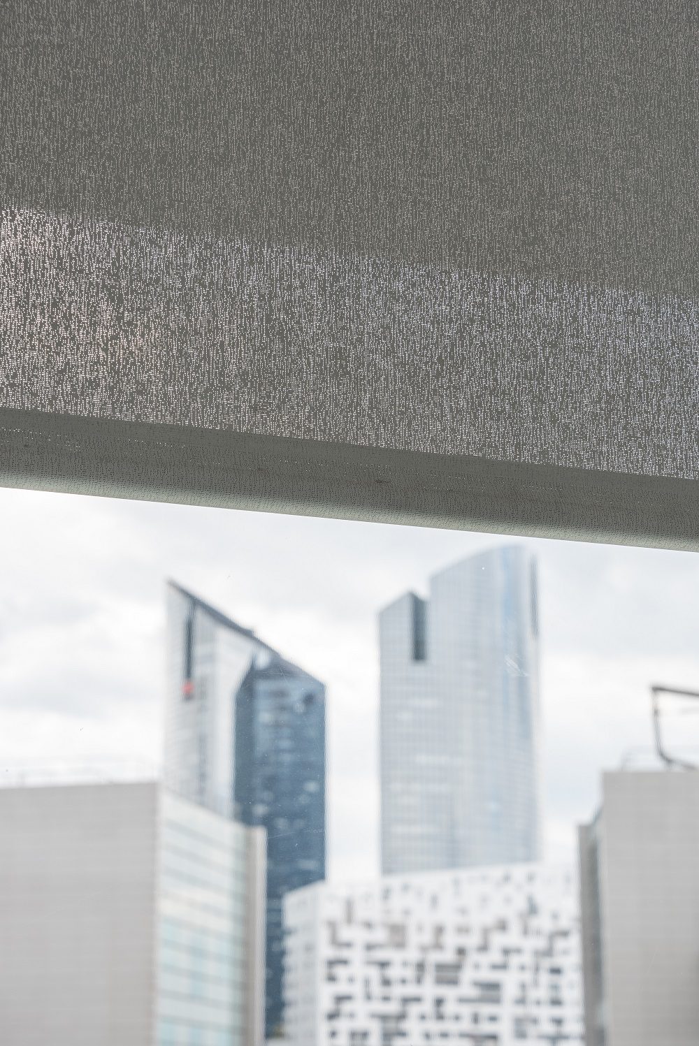 Gros plan sur une toile de store technique laissant filtrer la lumière avec vue urbaine en arrière-plan.