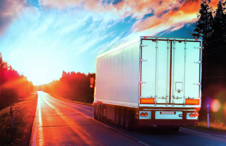 Camion de transport routier équipé d’une bâche en membrane technique tendue, roulant sur une route au coucher du soleil.
