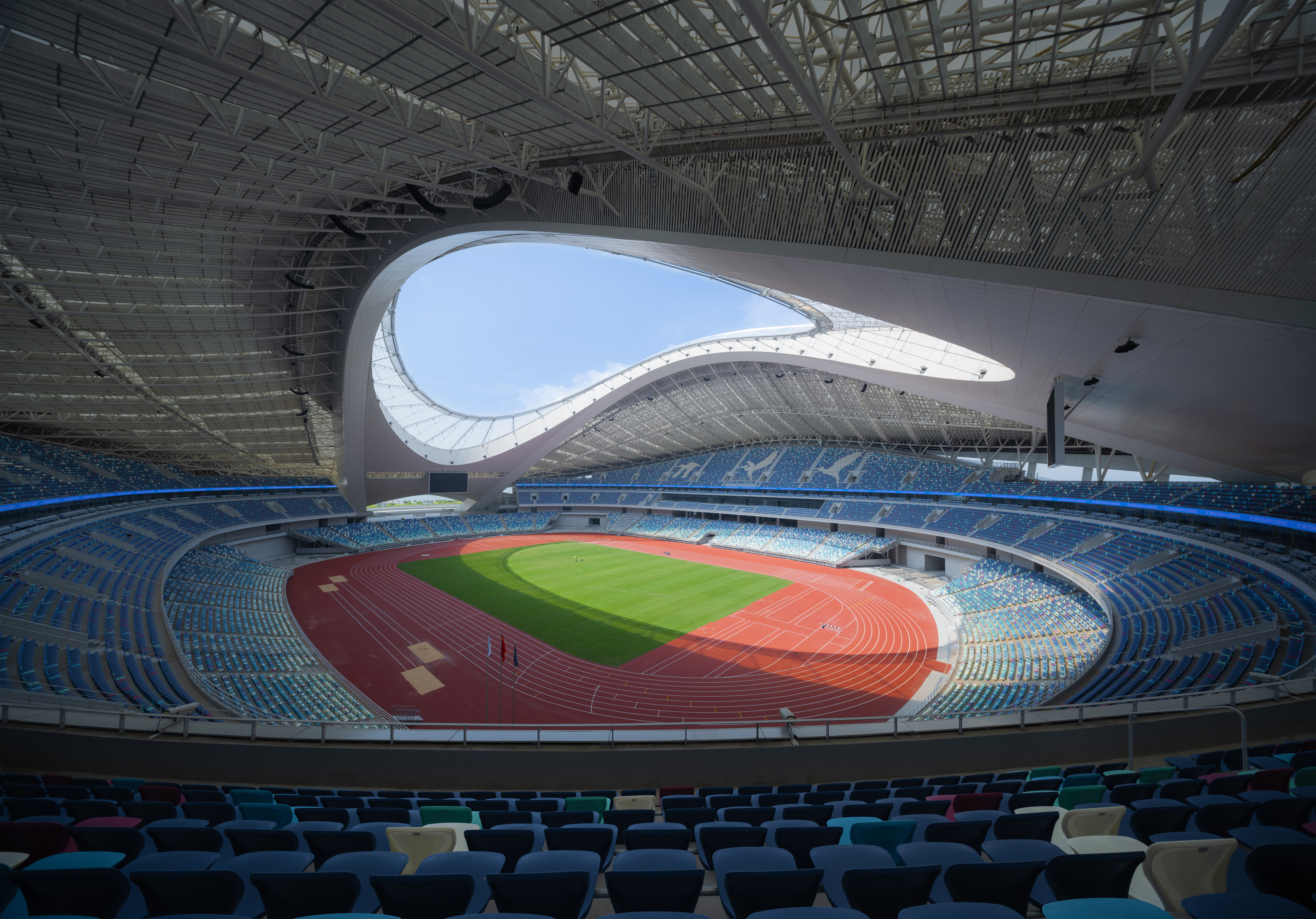 Vue intérieure du stade de Xiamen Bailu avec piste d’athlétisme, terrain central et toiture architecturale ajourée.