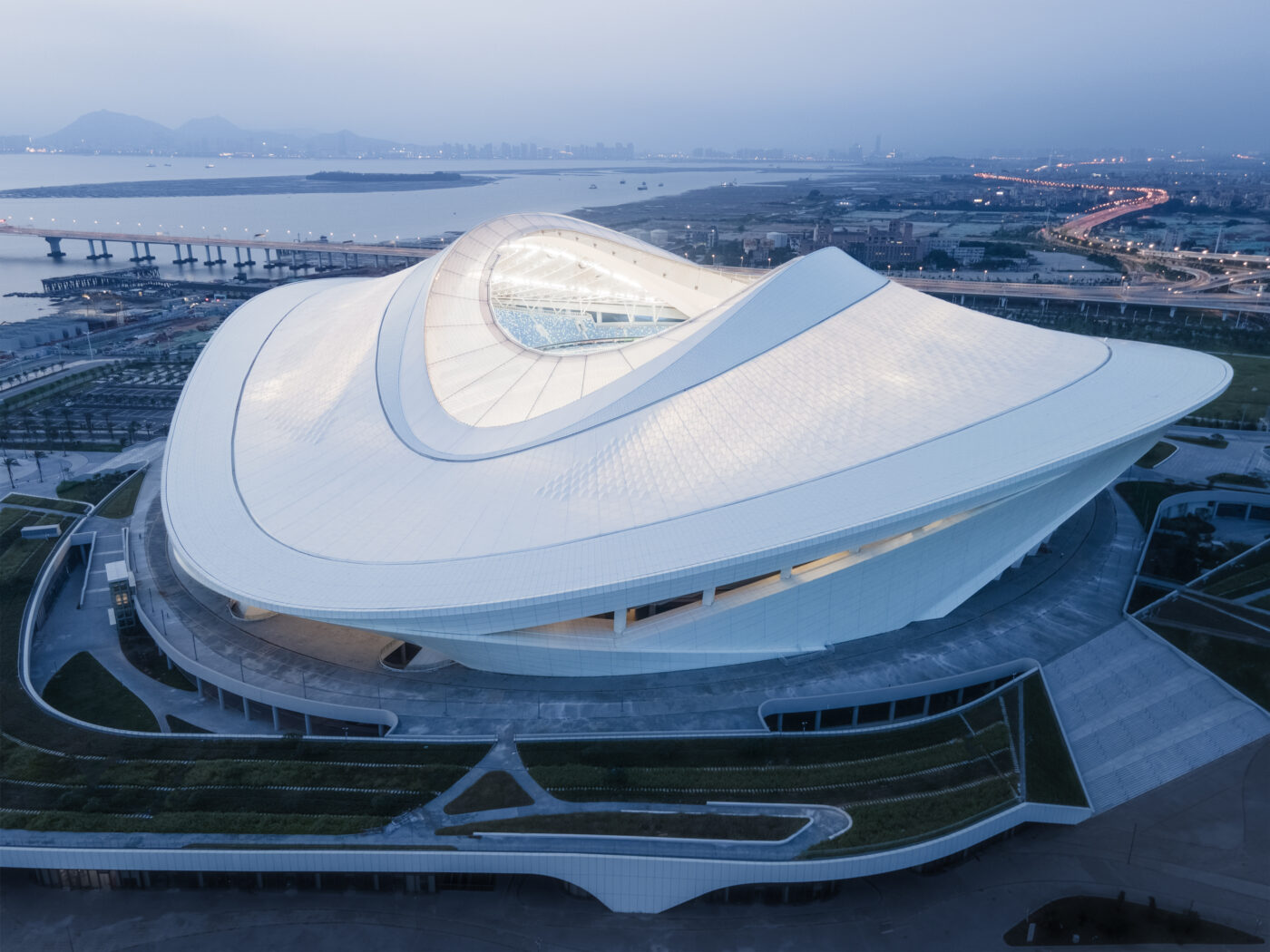 Vue aérienne du stade de Xiamen Bailu illuminé au crépuscule, mettant en valeur sa toiture blanche.