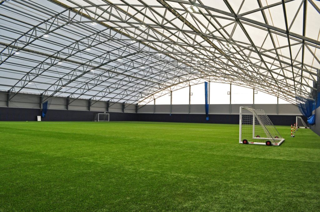 Halle sportive couverte avec toiture en membrane composite Serge Ferrari sur structure acier, lumière naturelle et terrain indoor.