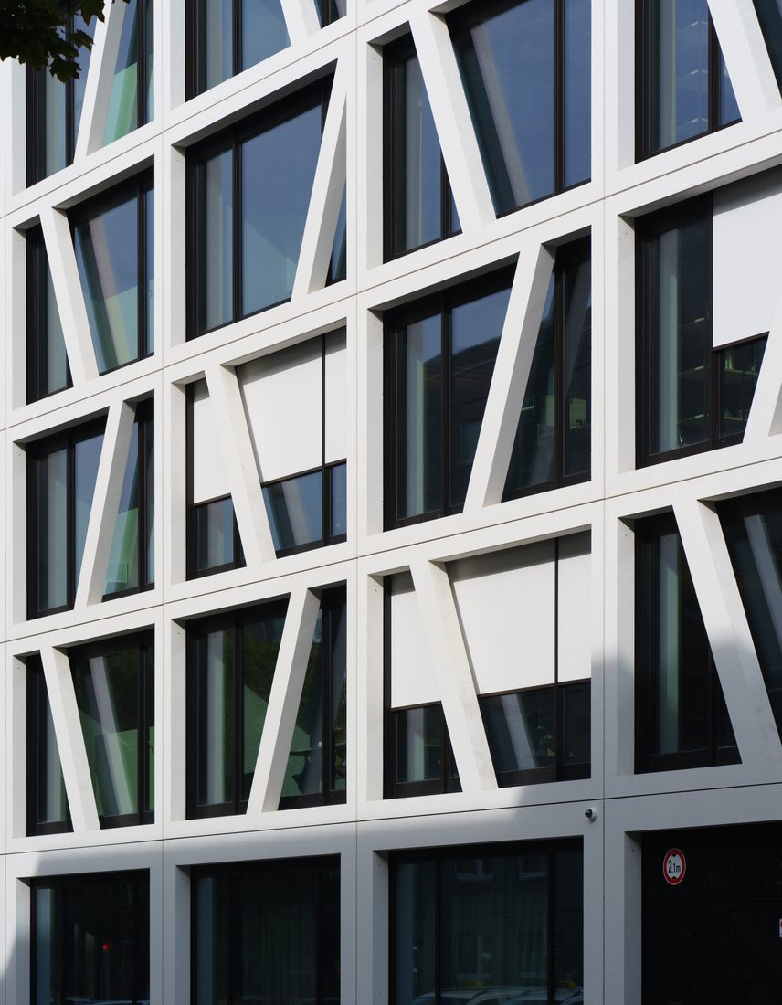 Détail de façade vitrée avec trame structurelle diagonale blanche.
