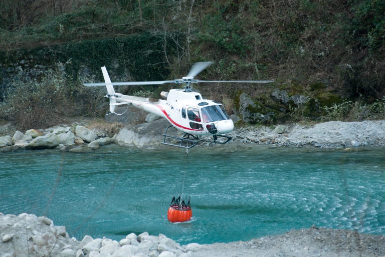 Hélicoptère puisant de l’eau avec un seau souple orange en membrane technique